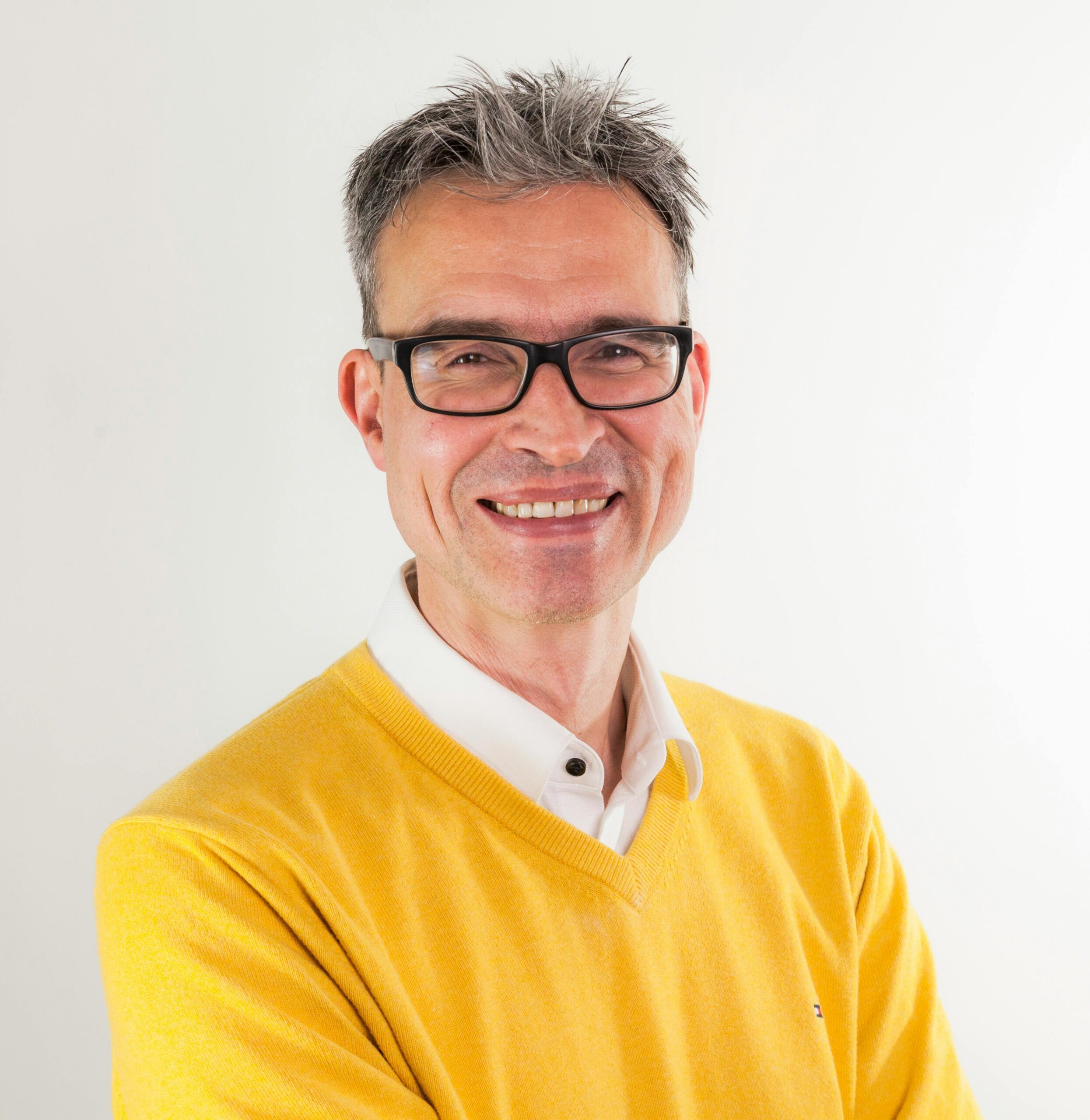 Confident adult man wearing glasses and yellow sweater, smiling at camera.