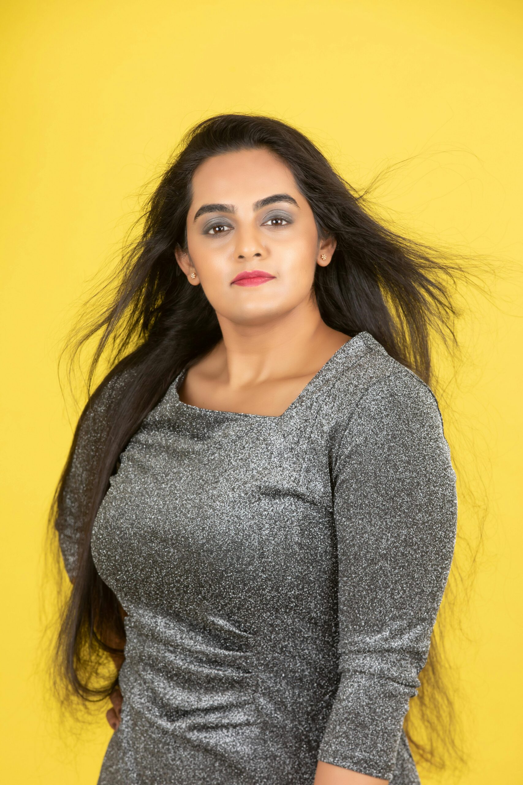 Portrait of a confident woman in a shimmering dress against a vibrant yellow backdrop.