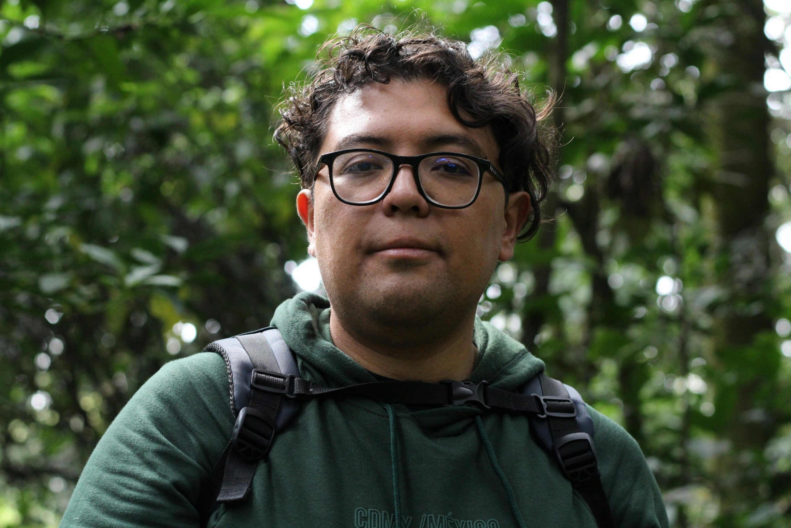 Portrait of a hiker surrounded by dense green jungle, wearing glasses and a green hoodie.