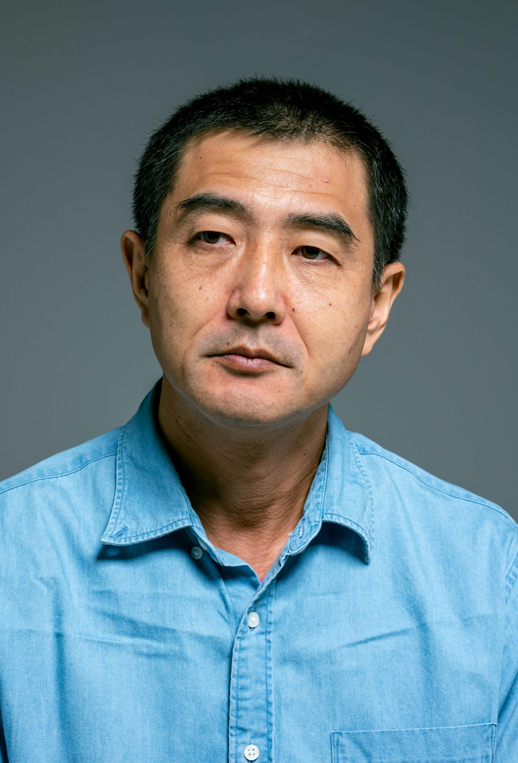 Studio portrait of a mature man in a blue shirt looking contemplative.