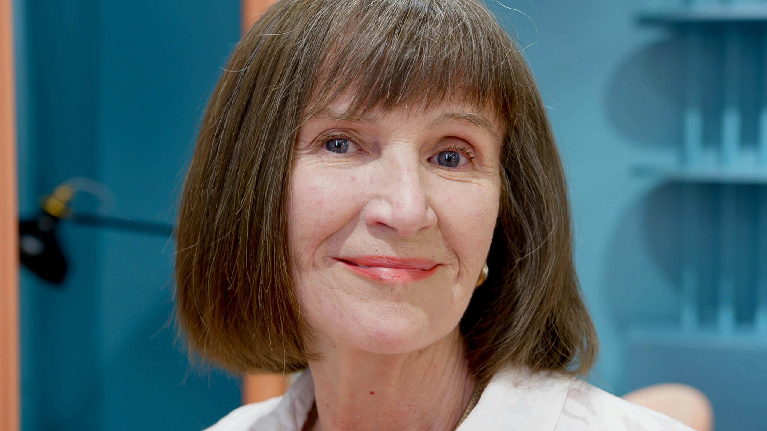 Portrait of a smiling senior woman with short brown hair indoors captured in a friendly close-up.